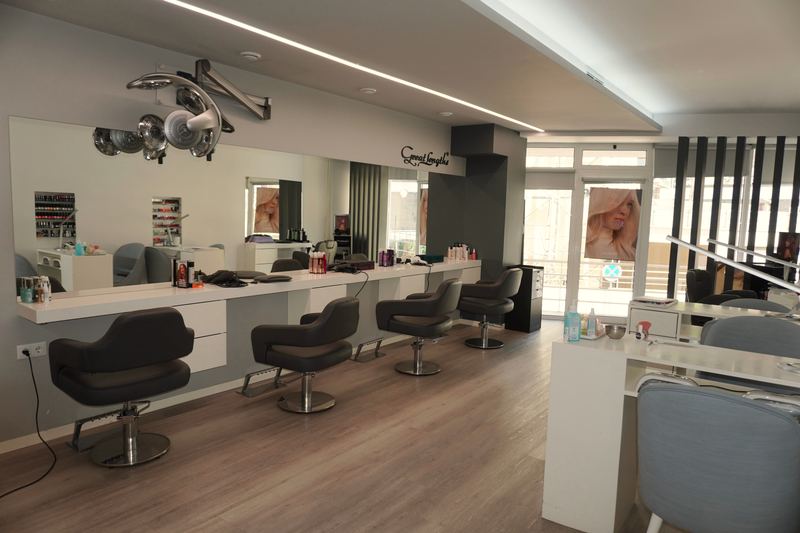 Zona de corte do salão: quatro cadeiras diante de um espelho corrido, com a receção ao fundo